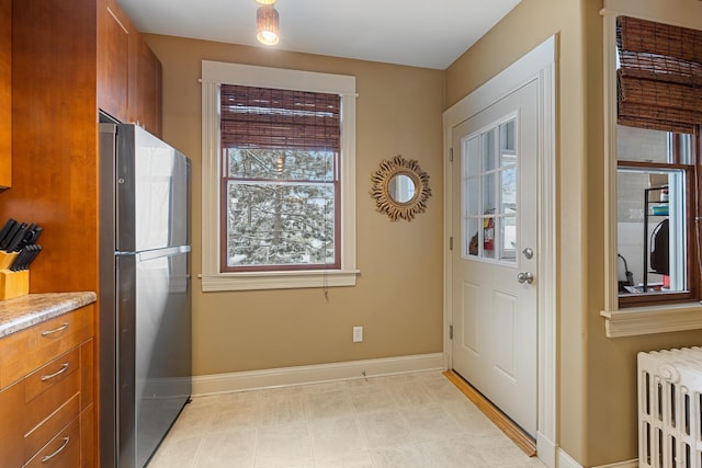 kitchen with baseboards, radiator, freestanding refrigerator, and brown cabinets