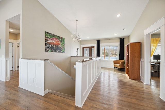 corridor with vaulted ceiling, an inviting chandelier, and light wood-type flooring