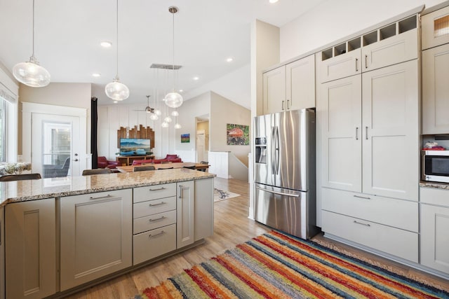 kitchen with lofted ceiling, stainless steel fridge, gray cabinetry, light stone countertops, and decorative light fixtures