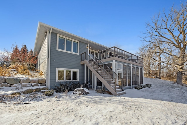 snow covered back of property featuring a sunroom