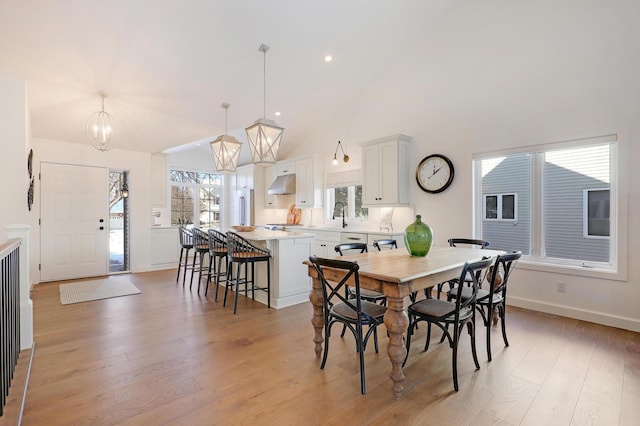 dining area featuring lofted ceiling, a notable chandelier, sink, and light hardwood / wood-style floors