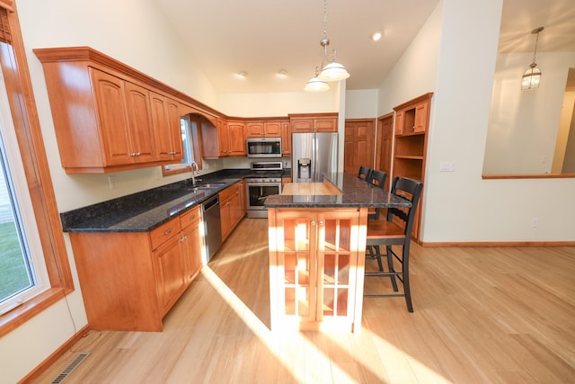 kitchen with stainless steel appliances, light wood-type flooring, a center island, hanging light fixtures, and sink