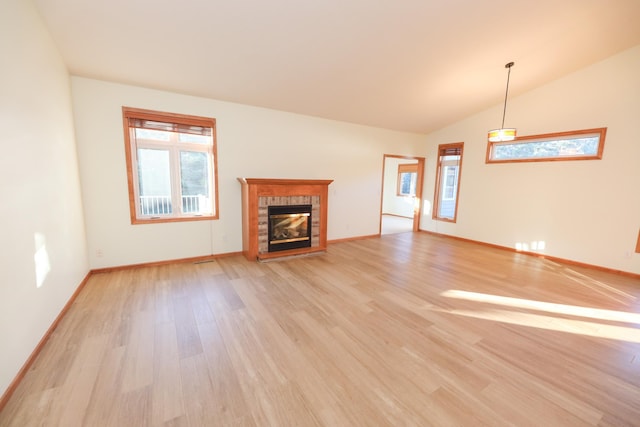 unfurnished living room featuring lofted ceiling, a tiled fireplace, light hardwood / wood-style flooring, and plenty of natural light