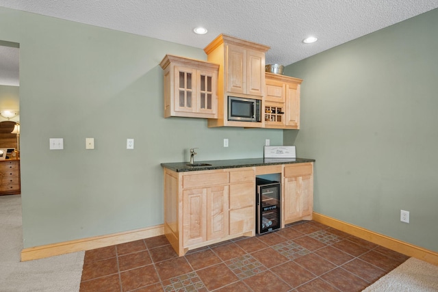 kitchen featuring sink, stainless steel microwave, a textured ceiling, beverage cooler, and light brown cabinets