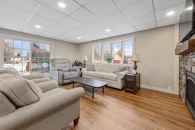 living room with a stone fireplace, light hardwood / wood-style flooring, and a paneled ceiling