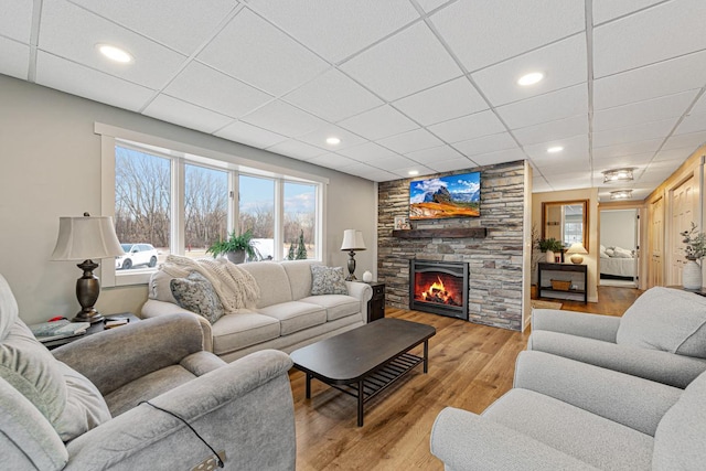 living room with a paneled ceiling, a stone fireplace, and light hardwood / wood-style floors