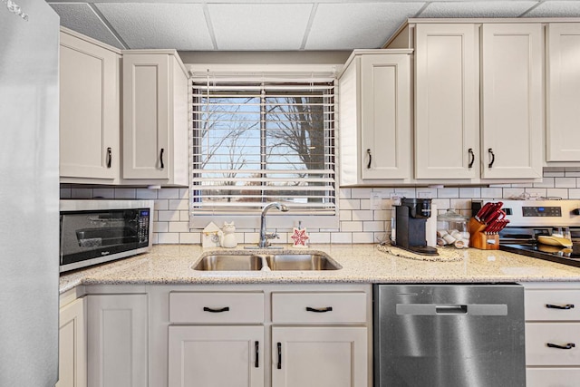 kitchen with sink, white cabinetry, light stone counters, appliances with stainless steel finishes, and decorative backsplash