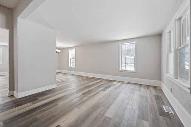 empty room with a healthy amount of sunlight, a notable chandelier, and hardwood / wood-style flooring