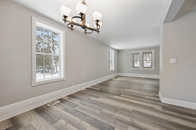 unfurnished dining area with an inviting chandelier, wood-type flooring, and a healthy amount of sunlight