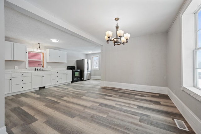 interior space with electric range, stainless steel fridge, sink, white cabinetry, and an inviting chandelier