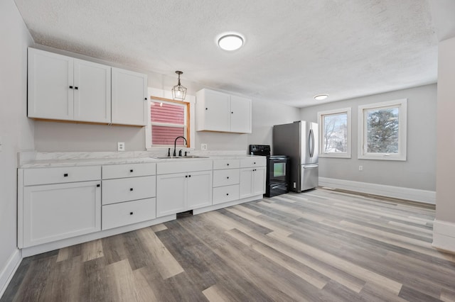 kitchen with hanging light fixtures, electric range, stainless steel refrigerator, white cabinets, and sink