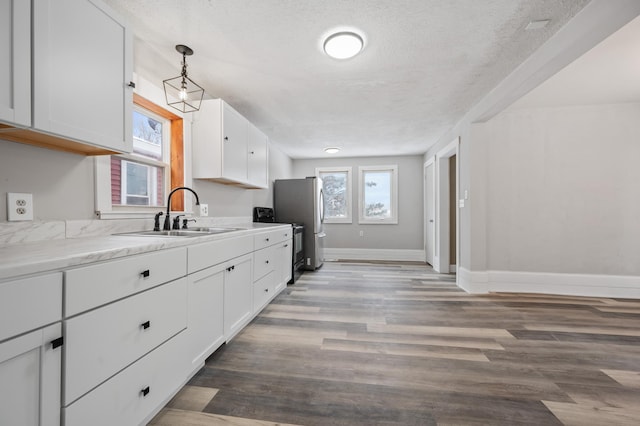 kitchen with sink, white cabinets, a textured ceiling, hanging light fixtures, and light stone countertops