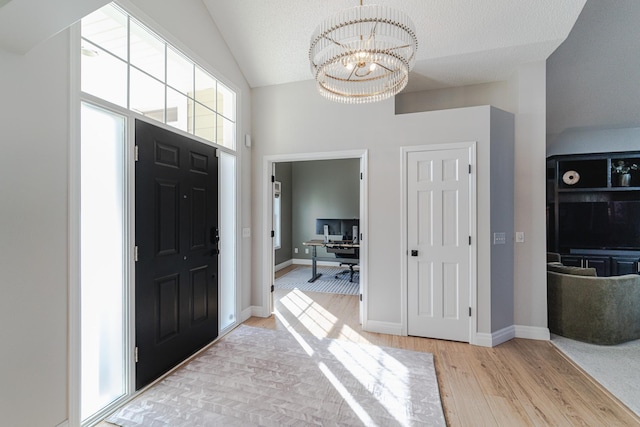 foyer with a textured ceiling, vaulted ceiling, light hardwood / wood-style flooring, and a notable chandelier