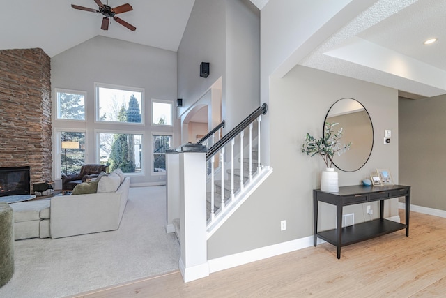 stairs featuring wood-type flooring, high vaulted ceiling, ceiling fan, and a fireplace