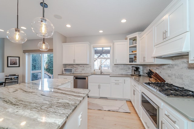 kitchen with pendant lighting, premium range hood, white cabinetry, appliances with stainless steel finishes, and light stone countertops