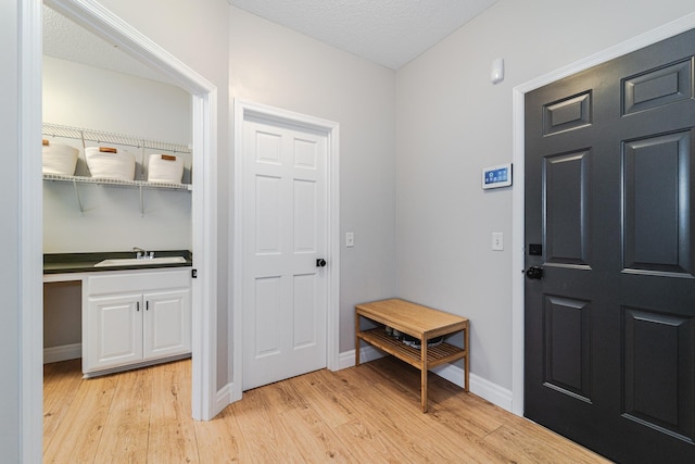 foyer entrance with sink, a textured ceiling, and light wood-type flooring