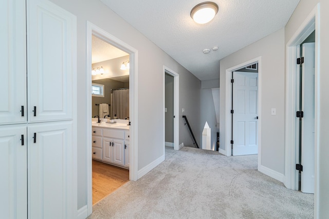 hall featuring sink, light colored carpet, and a textured ceiling