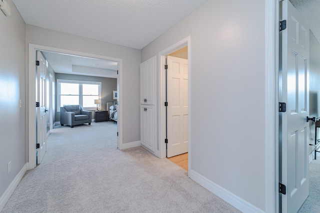 hall with light carpet and a textured ceiling