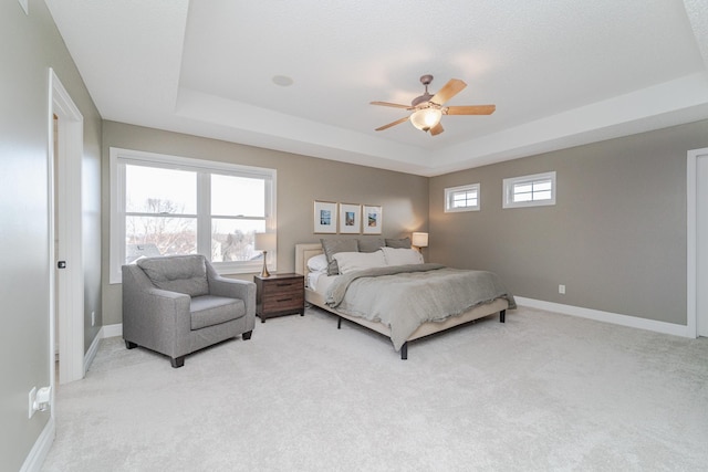 carpeted bedroom with multiple windows, ceiling fan, and a tray ceiling