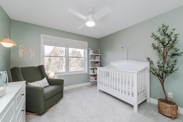 bedroom with a crib, light colored carpet, and ceiling fan