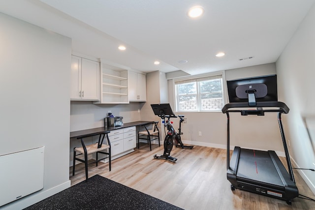 exercise room with built in desk and light wood-type flooring