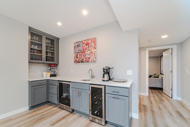 bar featuring beverage cooler, sink, and light hardwood / wood-style flooring