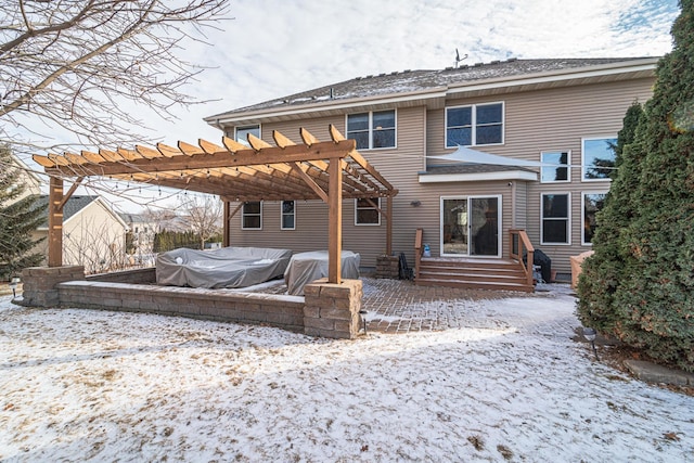 snow covered back of property with a pergola and a patio area