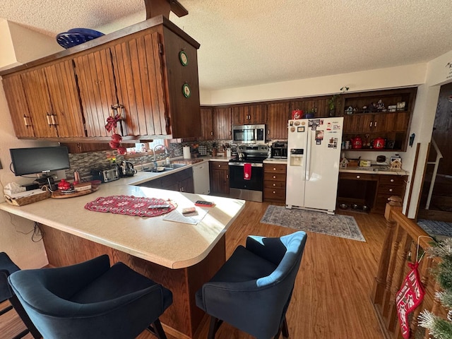 kitchen with a textured ceiling, appliances with stainless steel finishes, light hardwood / wood-style floors, sink, and kitchen peninsula