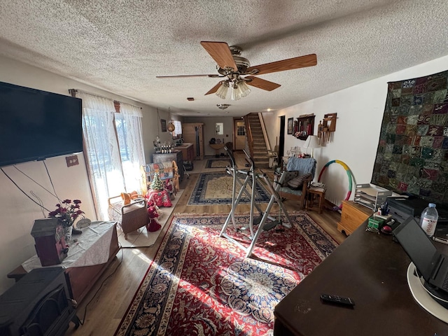 interior space with a textured ceiling, ceiling fan, a wood stove, and hardwood / wood-style flooring