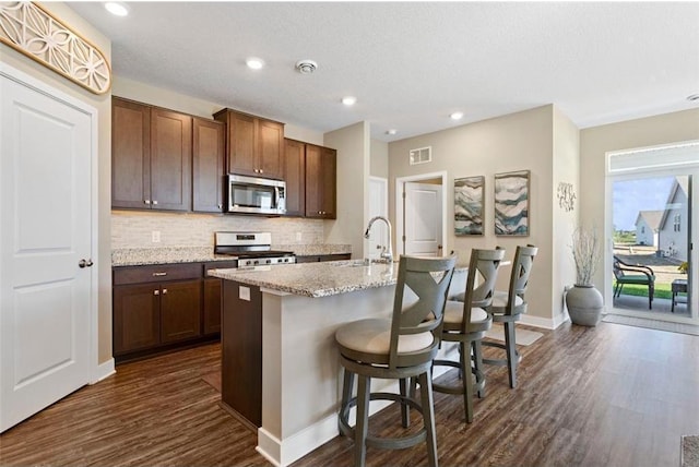 kitchen with a kitchen bar, stainless steel appliances, tasteful backsplash, dark hardwood / wood-style floors, and a center island with sink