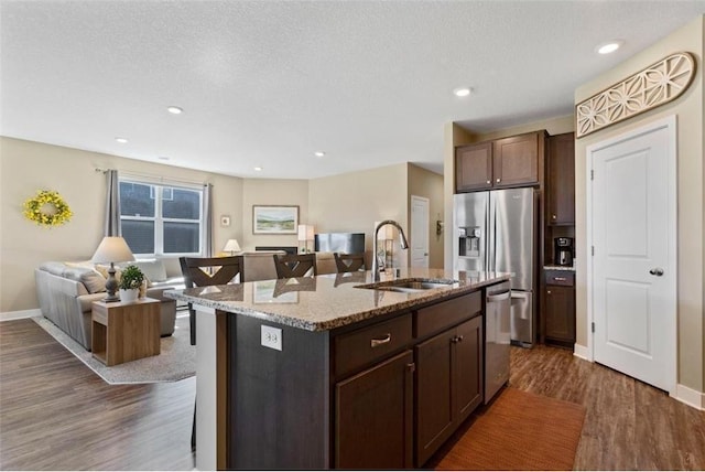 kitchen with a kitchen breakfast bar, dark hardwood / wood-style flooring, sink, a kitchen island with sink, and stainless steel appliances