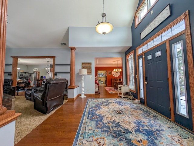 foyer featuring hardwood / wood-style flooring, crown molding, decorative columns, and a notable chandelier