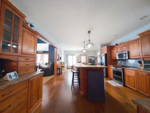 kitchen featuring dark wood-type flooring, a breakfast bar, appliances with stainless steel finishes, hanging light fixtures, and a kitchen island