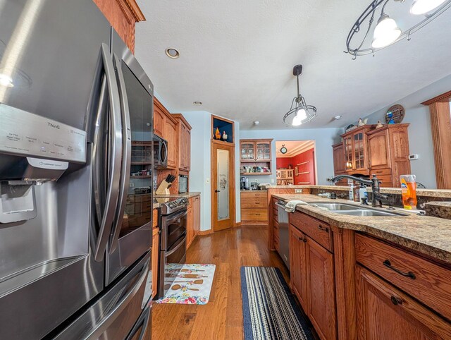 kitchen with sink, stainless steel appliances, light stone counters, light hardwood / wood-style floors, and decorative light fixtures