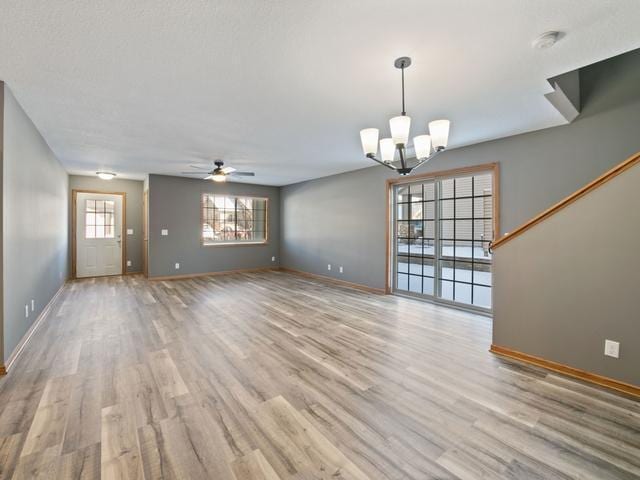 unfurnished living room with ceiling fan with notable chandelier and light hardwood / wood-style flooring