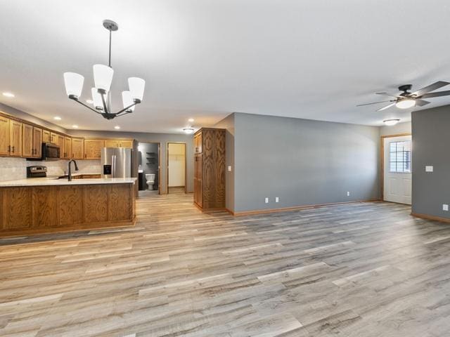 kitchen featuring kitchen peninsula, ceiling fan with notable chandelier, light hardwood / wood-style flooring, hanging light fixtures, and appliances with stainless steel finishes