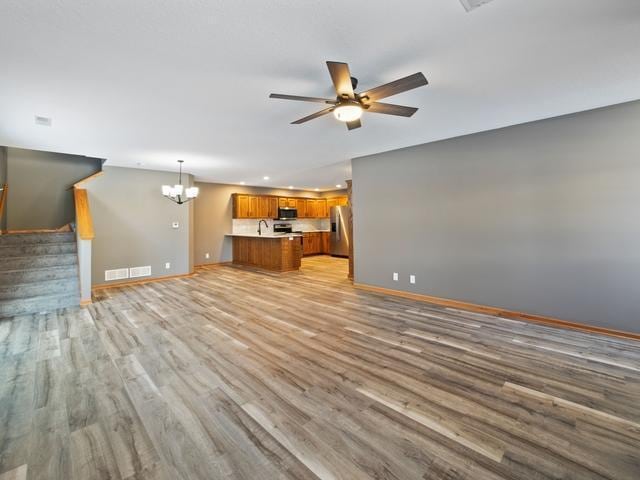 unfurnished living room featuring light hardwood / wood-style flooring and ceiling fan with notable chandelier