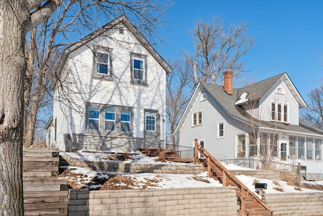 snow covered property featuring stairs, a sunroom, and a chimney