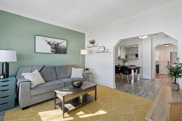 living room featuring baseboards, ornamental molding, wood finished floors, arched walkways, and a textured ceiling