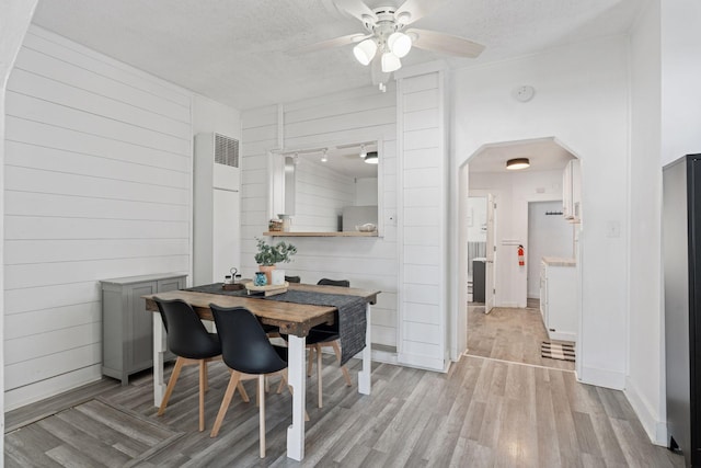 dining room featuring baseboards, light wood-style floors, arched walkways, and a textured ceiling