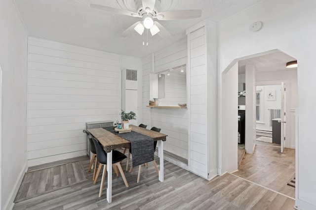 dining area with a ceiling fan, wooden walls, wood finished floors, and arched walkways