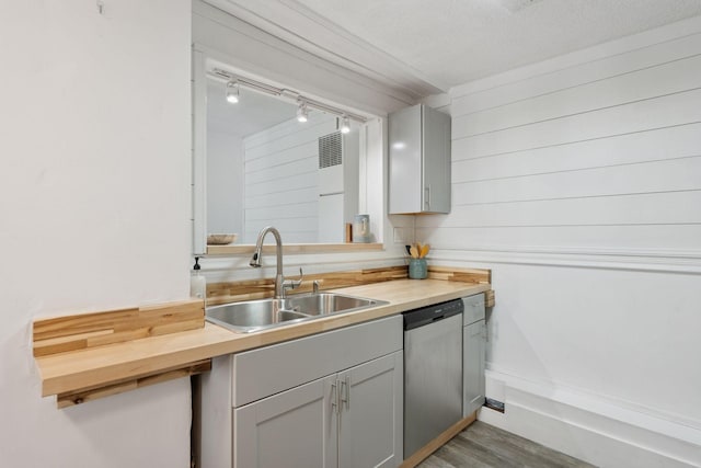 kitchen with a sink, stainless steel dishwasher, wood finished floors, rail lighting, and butcher block counters