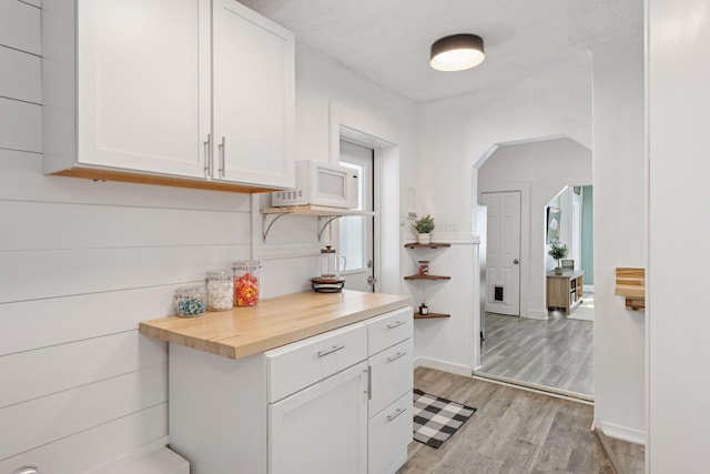 kitchen with white microwave, baseboards, light wood-type flooring, white cabinets, and wood counters