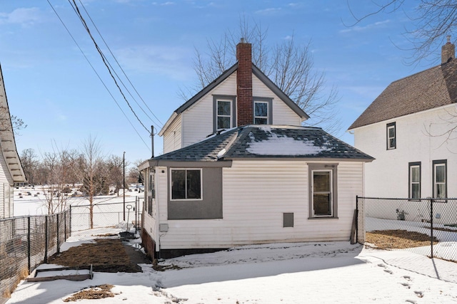 snow covered back of property with a chimney, a fenced backyard, and roof with shingles