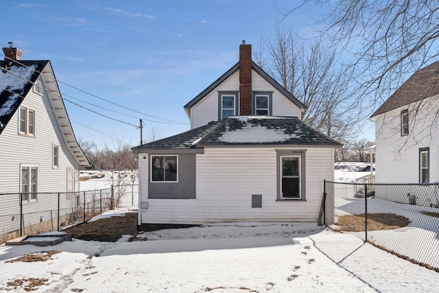 snow covered rear of property featuring a chimney, roof with shingles, and fence