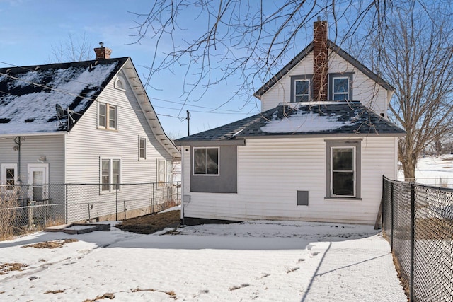 snow covered house with a fenced backyard and a chimney