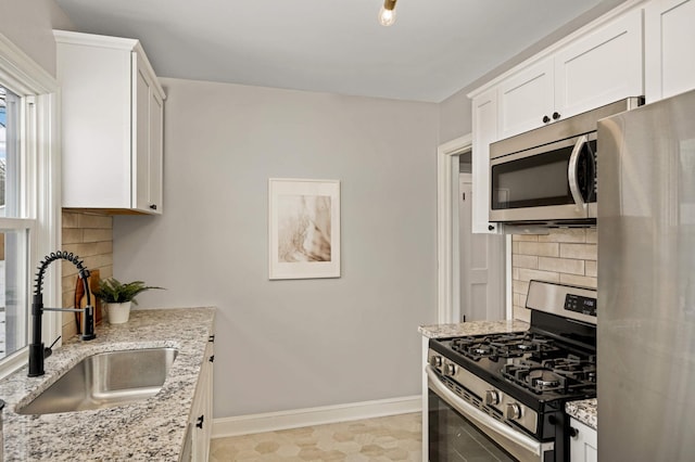 kitchen featuring light stone countertops, white cabinets, stainless steel appliances, decorative backsplash, and sink