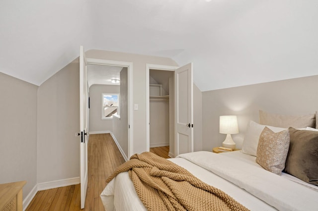 bedroom featuring vaulted ceiling, a closet, a walk in closet, and light wood-type flooring