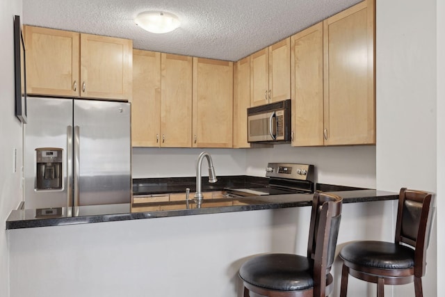 kitchen featuring stainless steel appliances, a kitchen breakfast bar, a textured ceiling, and light brown cabinets