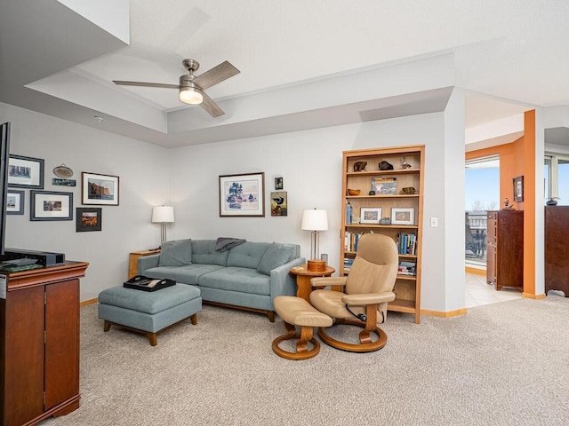 carpeted living room with ceiling fan and a tray ceiling